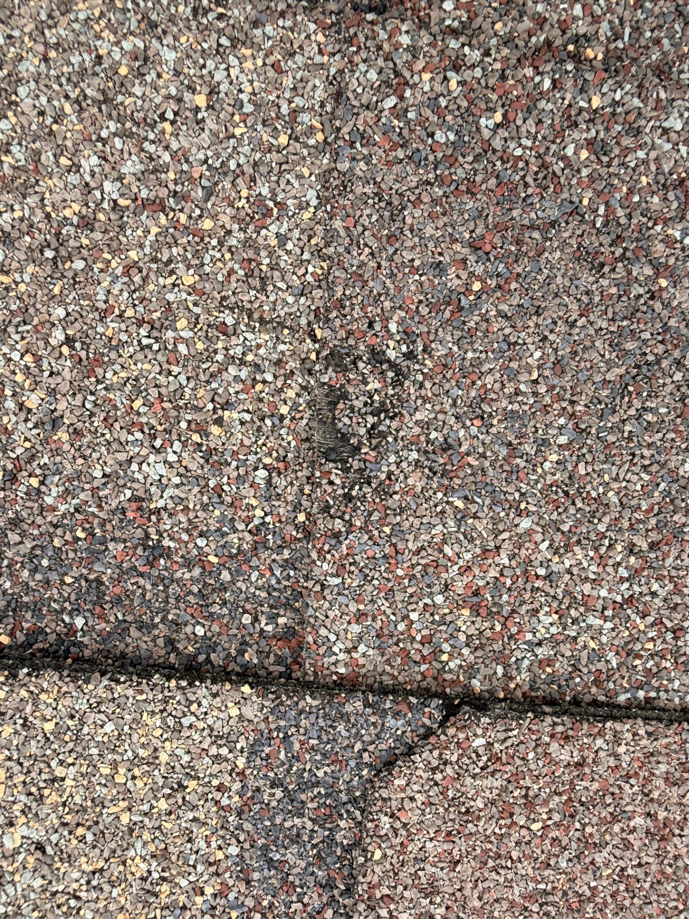 Inspection photo of hail damage along a shingle seam on a Moorhead roof, showing granule loss and exposed dark asphalt
