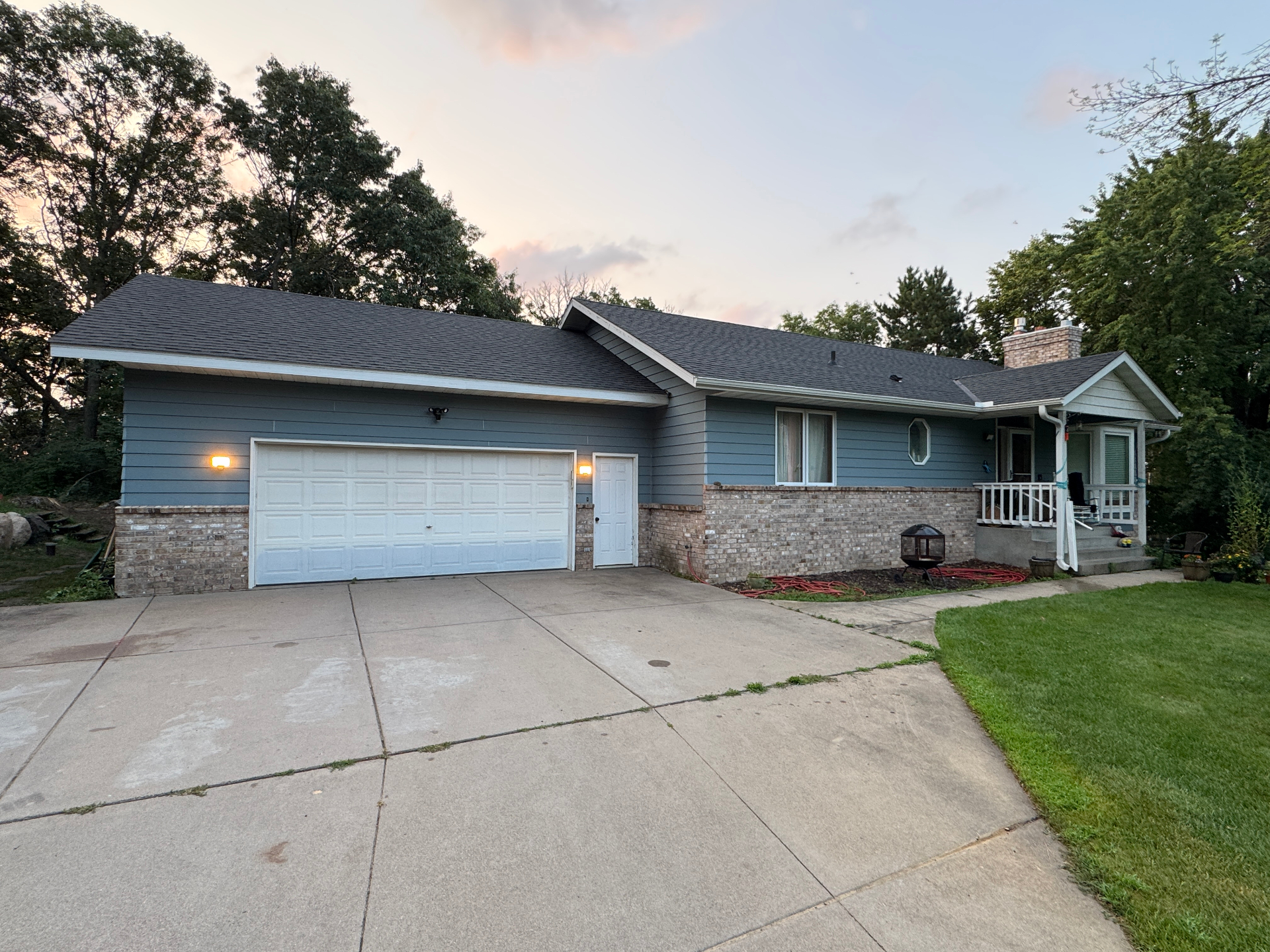 Elk River, MN home before the 2026 roofing and siding replacement, showing existing blue-gray siding, front brick, and an attached garage