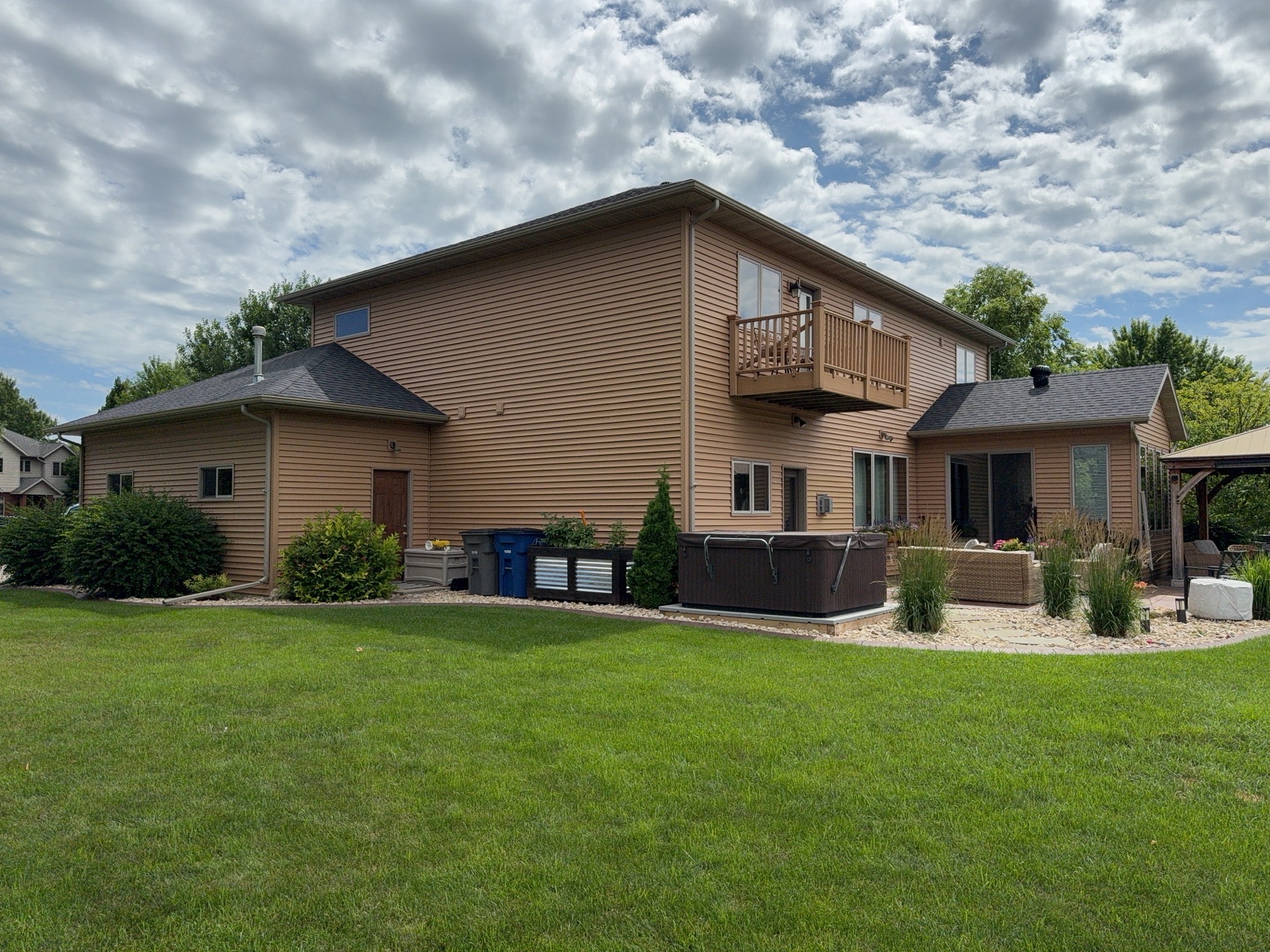 Rear elevation of a Moorhead, MN home with existing brown vinyl siding, a second-floor balcony, and a patio before insurance-covered siding replacement