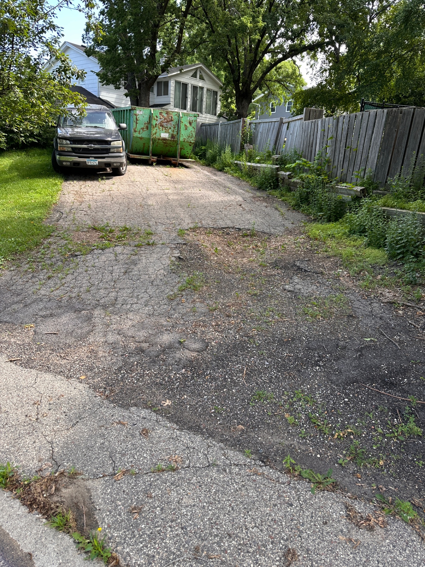 Old cracked and weed-covered asphalt driveway in the backyard of the Burnsville, MN home before replacement