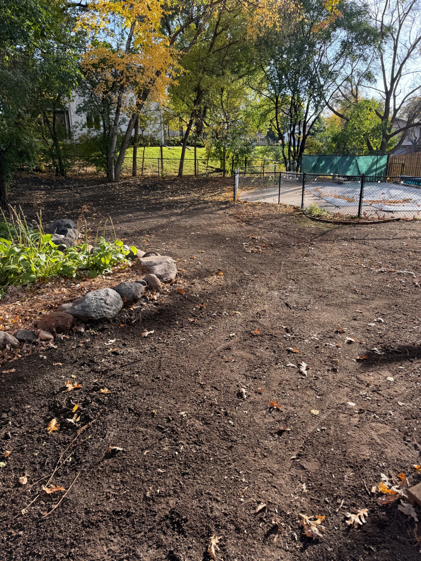 Cleared and regraded backyard with fresh topsoil and stone-edged planting bed after skid-loader renovation in Burnsville, MN