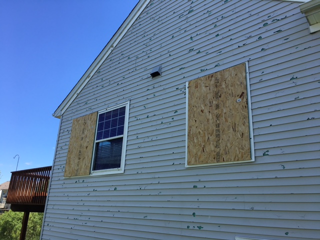 Blaine home with hail-pocked siding and boarded-up windows after a golf ball hail storm