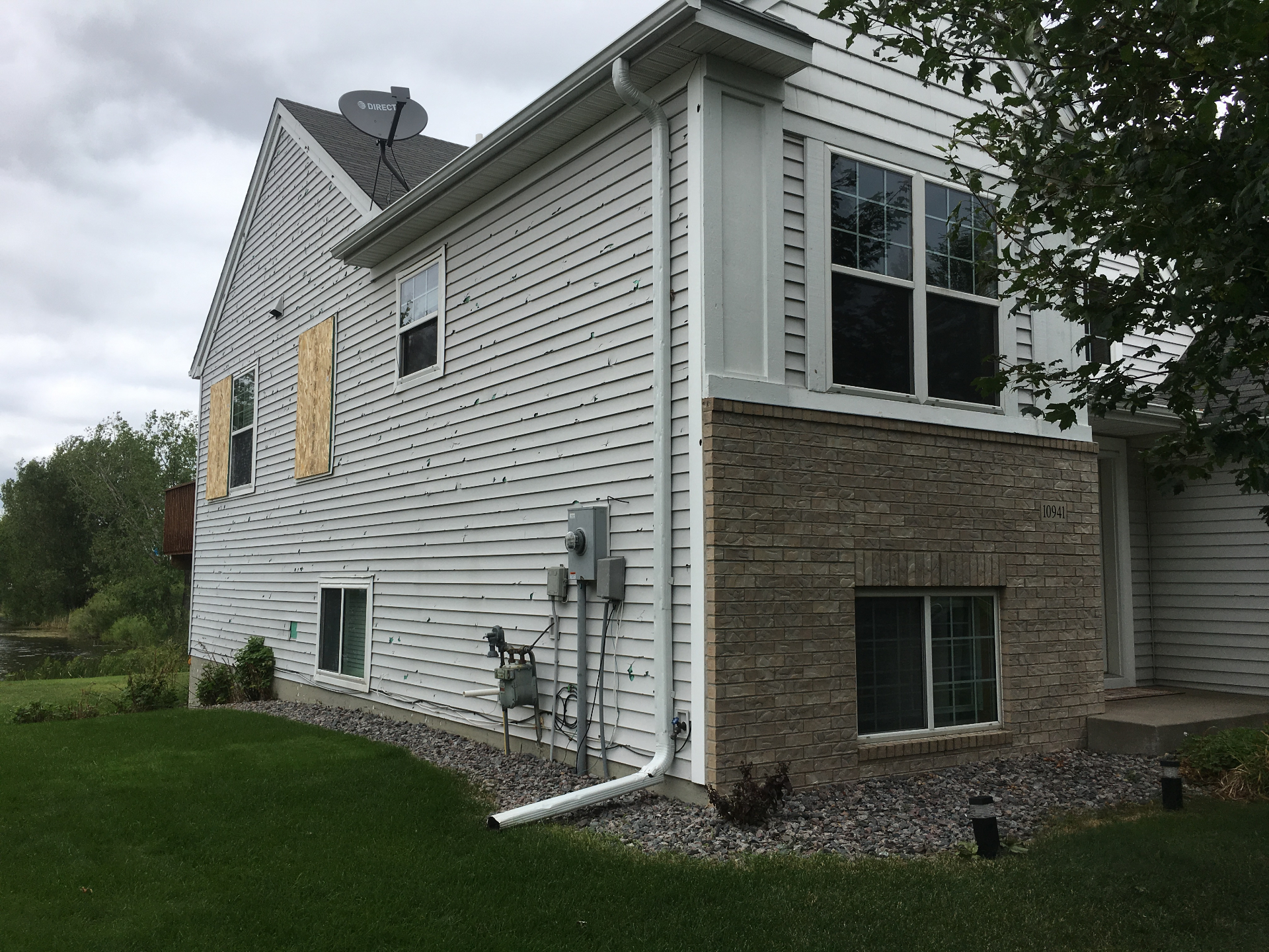 Wider view of the Blaine home showing hail damage across siding, gutters, and roof